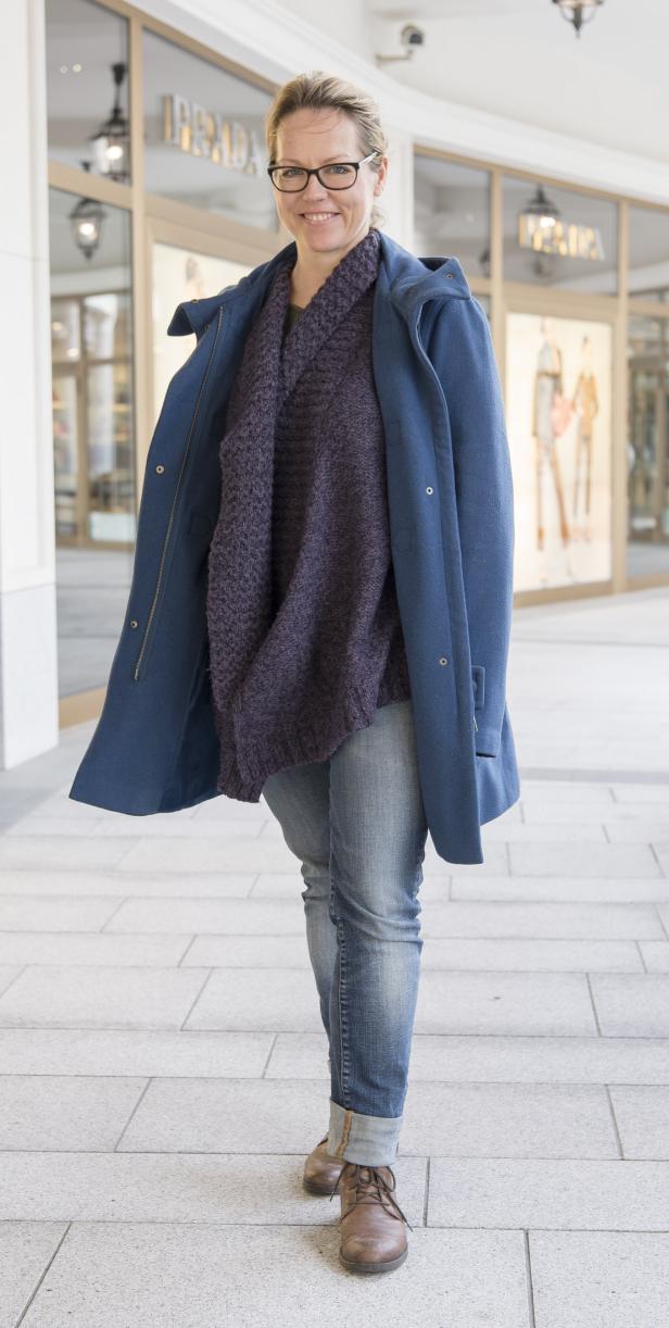 Eine Frau mit Brille, blauer Jacke und Jeans geht an einem Schaufenster von Prada vorbei.