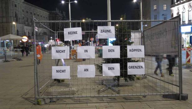 Ein Bauzaun mit Schildern, die zusammen den Satz „Keine Zäune. Nicht in den Köpfen. Nicht an den Grenzen.“ ergeben.