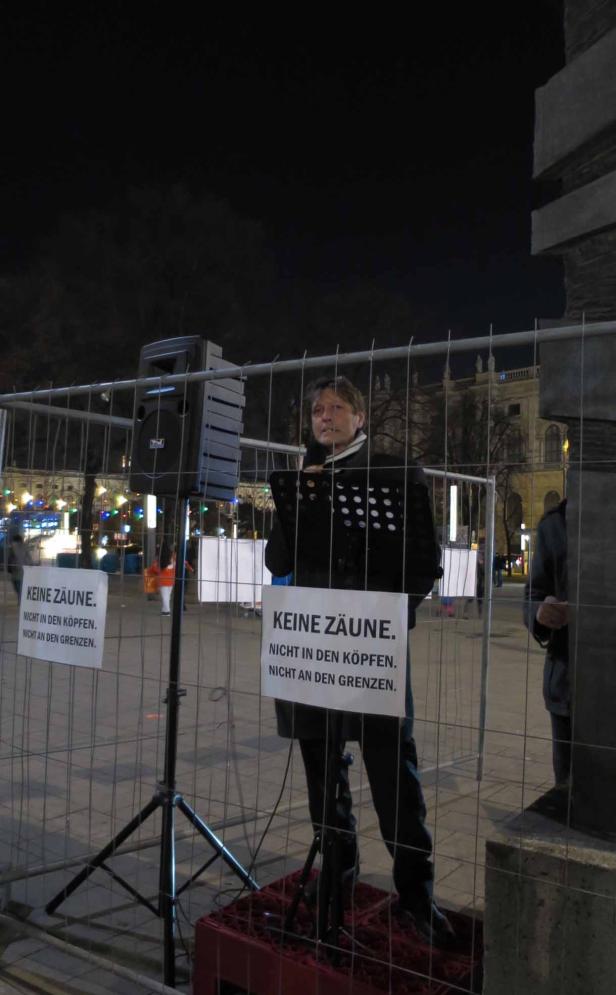 Eine Person steht hinter einem Zaun mit Schildern, die „Keine Zäune. Nicht in den Köpfen. Nicht an den Grenzen.“ zeigen.