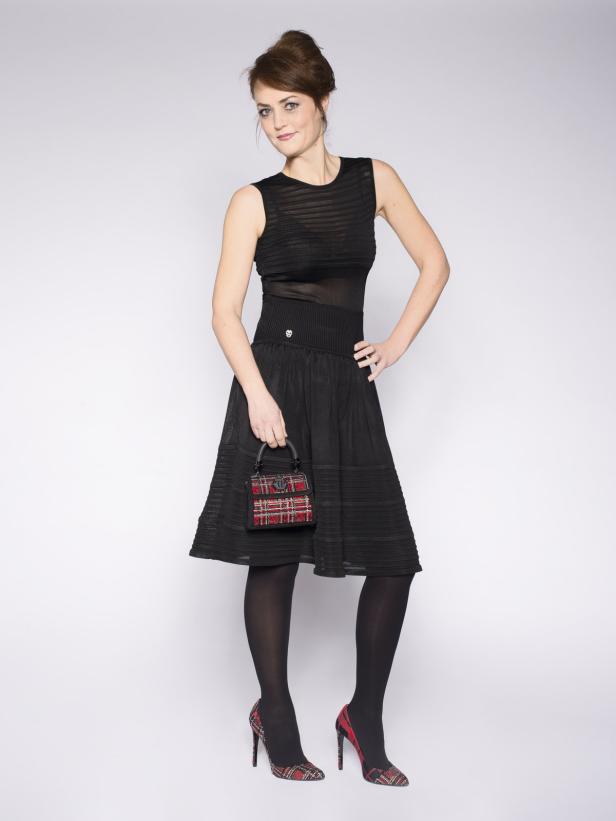 Eine Frau in einem schwarzen Kleid mit einer karierten Handtasche und passenden Schuhen.