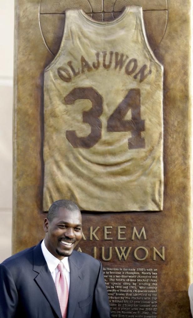 Hakeem Olajuwon vor einem Denkmal mit seinem Trikot mit der Nummer 34.