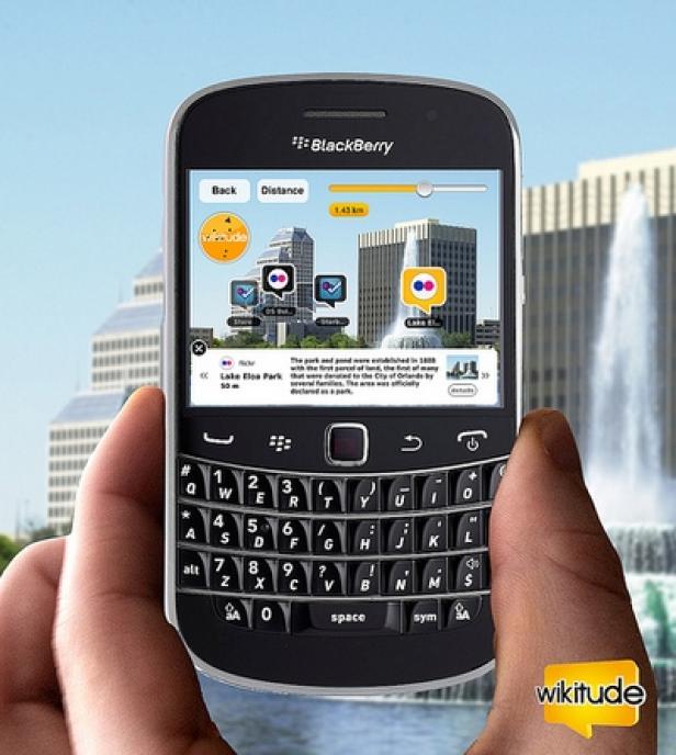 Eine Hand hält ein BlackBerry-Smartphone mit einer Augmented-Reality-App vor einem Brunnen.