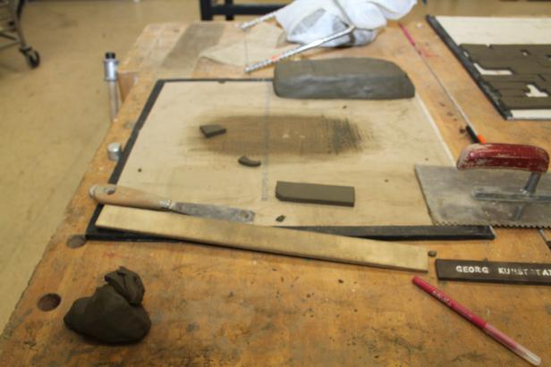 Ein Arbeitstisch mit Ton, Werkzeugen und einer Inschrift „Georg Kunststat“.