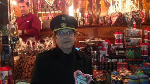 Ein Mann in Uniform hält ein Lebkuchenherz vor einem Stand mit Weihnachtsleckereien.