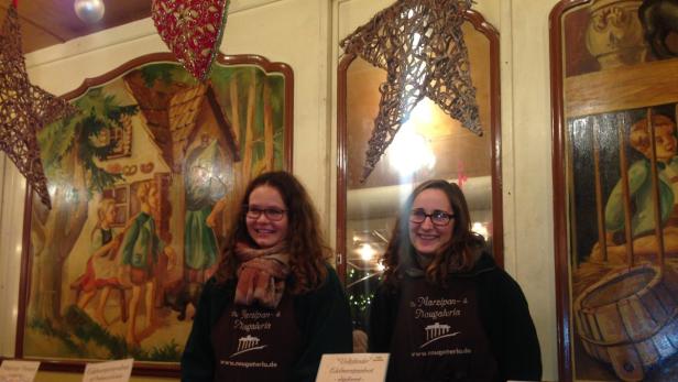 Zwei Frauen stehen vor bemalten Tafeln und tragen Schürzen der Marzipan- & Nougateria.