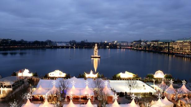 Blick auf den Hamburger Weihnachtsmarkt auf der Alster mit einem beleuchteten Weihnachtsbaum im Wasser.