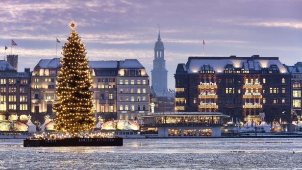 Ein Weihnachtsbaum auf einem Ponton vor der Skyline von Hamburg mit weihnachtlicher Beleuchtung.