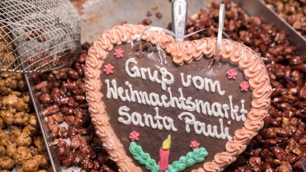 Ein Lebkuchenherz mit der Aufschrift „Gruß vom Weihnachtsmarkt Santa Pauli“ liegt neben gebrannten Mandeln.