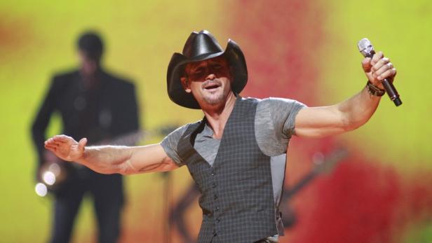 Tim McGraw tritt mit Cowboyhut und Mikrofon auf einer Bühne auf.