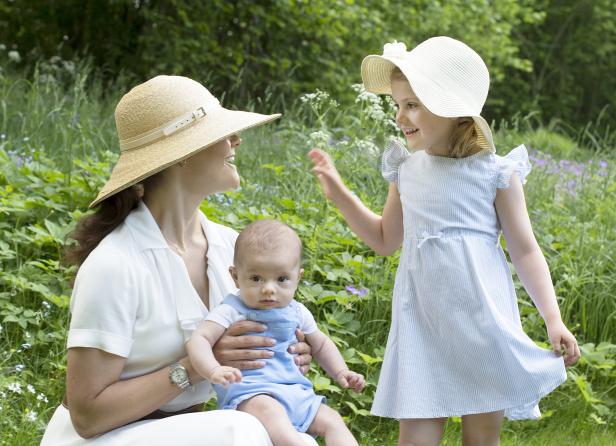 Eine Frau mit Hut hält ein Baby, während ein kleines Mädchen daneben steht.