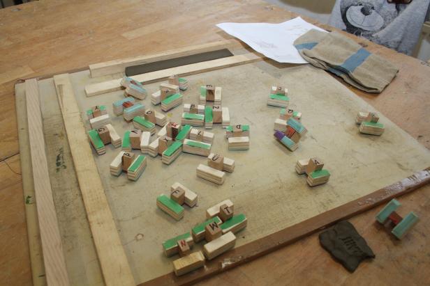Auf einem Tisch liegen Holzklötze mit Buchstaben, Werkzeuge und eine Anleitung.