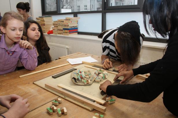Schülerinnen arbeiten mit Holz und kleinen bedruckten Blöcken an einem Tisch.