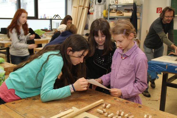 Schülerinnen arbeiten in einem Werkraum mit Holzbuchstaben an einem Projekt.
