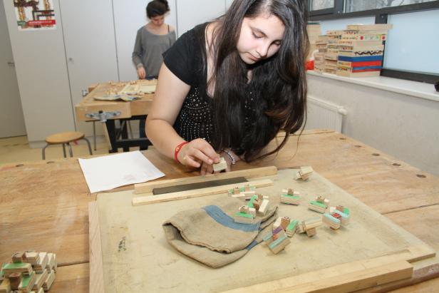Eine junge Frau arbeitet mit Holzbausteinen in einer Werkstatt.