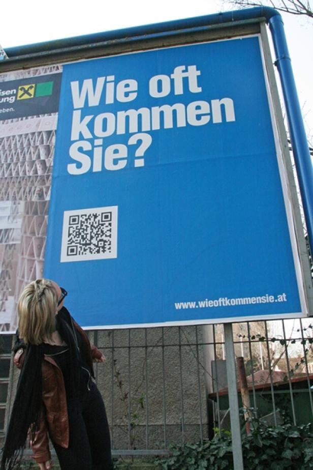 Eine Frau betrachtet ein blaues Plakat mit der Aufschrift „Wie oft kommen Sie?“.
