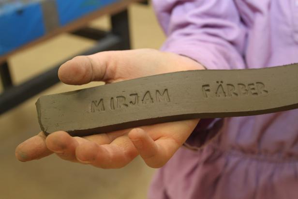 Eine Hand hält einen Tonstreifen mit den eingeprägten Namen „Mirjam Färber“.