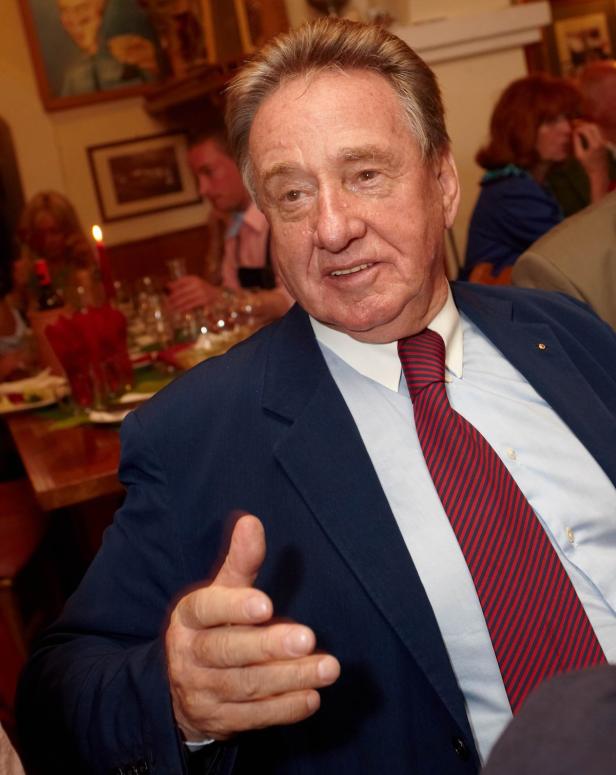 Ein Mann im Anzug gestikuliert bei einem Abendessen.