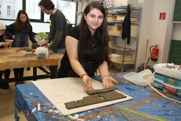 Eine junge Frau arrangiert beschriftete Tonziegel auf einer Platte in einem Werkraum.