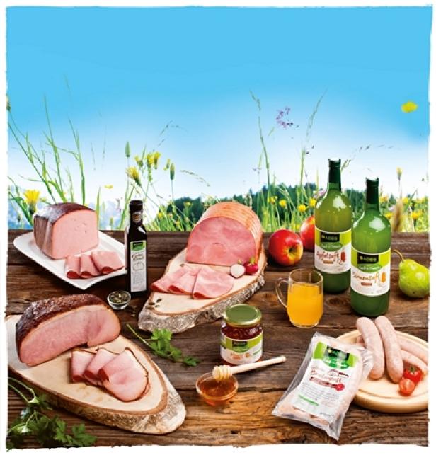Aufschnitt, Wurst, Apfelsaft und andere Produkte auf einem Holztisch im Freien.