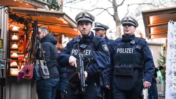 Polizisten mit Maschinenpistolen stehen auf einem Weihnachtsmarkt.