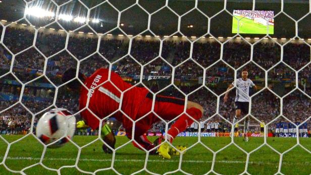 Ein Fußball landet im Netz, während der Torwart sich vergeblich streckt.