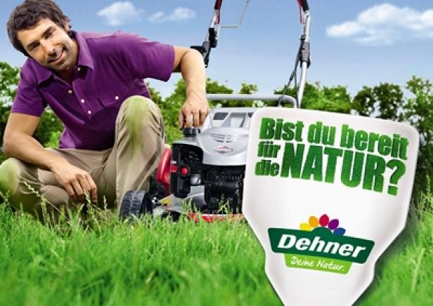 Ein Mann startet einen Rasenmäher in einem Garten, daneben ein Dehner-Werbeschild.