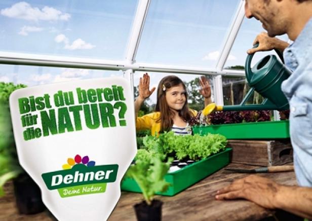 Ein Vater gießt mit seiner Tochter im Gewächshaus Salatpflanzen.