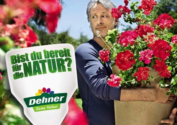 Ein Mann hält einen Topf mit roten Geranien in den Armen.