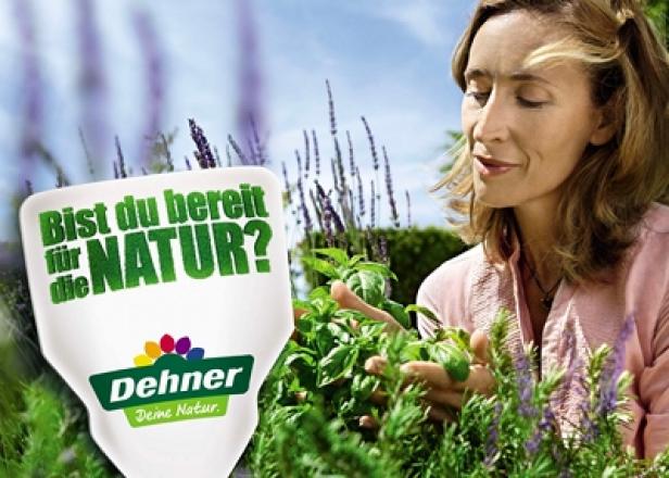 Eine Frau riecht an Basilikum in einem Garten, im Vordergrund ein Dehner-Logo.