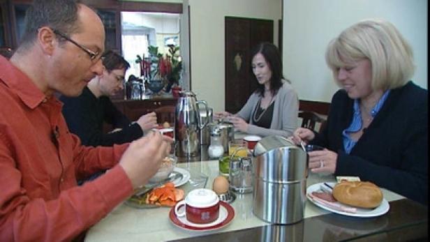 Vier Personen sitzen an einem Tisch und frühstücken.