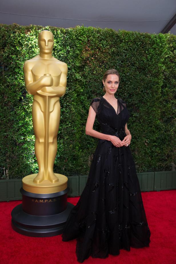 Angelina Jolie posiert neben einer Oscar-Statue auf dem roten Teppich.