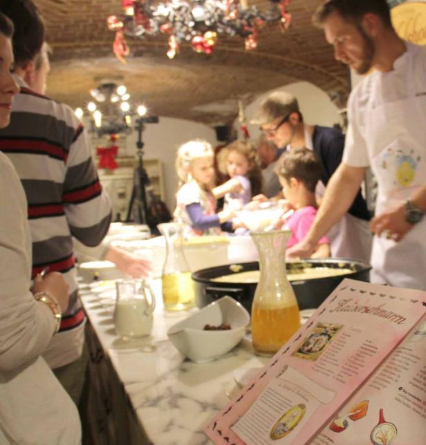 Kinder bereiten mit Erwachsenen Kaiserschmarrn in einer Küche zu.