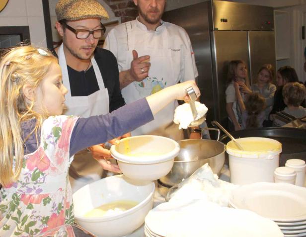 Ein Mädchen hilft mit Anleitung beim Zubereiten von Crêpes in einer Küche.