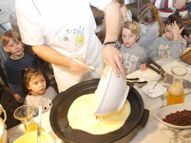 Ein Koch bereitet mit einer Gruppe von Kindern Pfannkuchen zu.