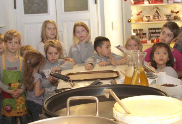 Eine Gruppe von Kindern steht um eine Küche herum und bereitet Crêpes zu.