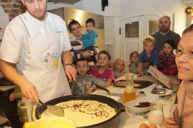 Ein Koch bereitet mit einer Gruppe von Kindern einen großen Pfannkuchen zu.