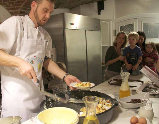 Ein Koch bereitet Kaiserschmarrn vor, während einige Kinder und Frauen zusehen.
