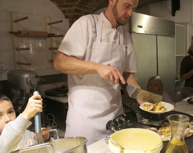 Ein Koch serviert Kaiserschmarrn, während Kinder in der Küche helfen.