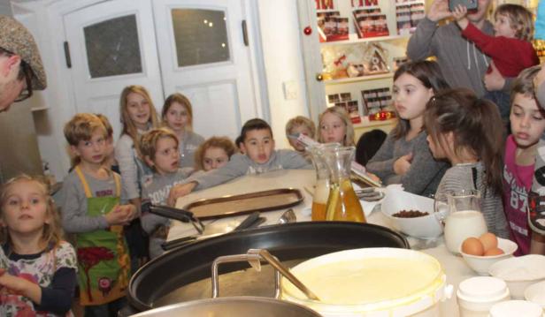 Eine Gruppe Kinder beobachtet aufmerksam die Zubereitung von Crêpes.