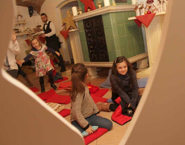 Kinder sitzen und spielen in einem weihnachtlich geschmückten Raum.