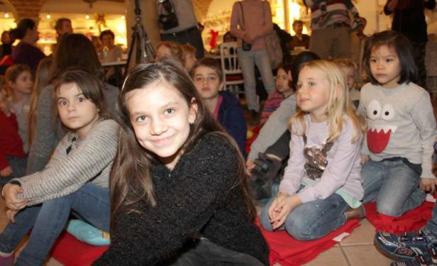 Eine Gruppe von Kindern sitzt auf dem Boden und schaut aufmerksam zu.