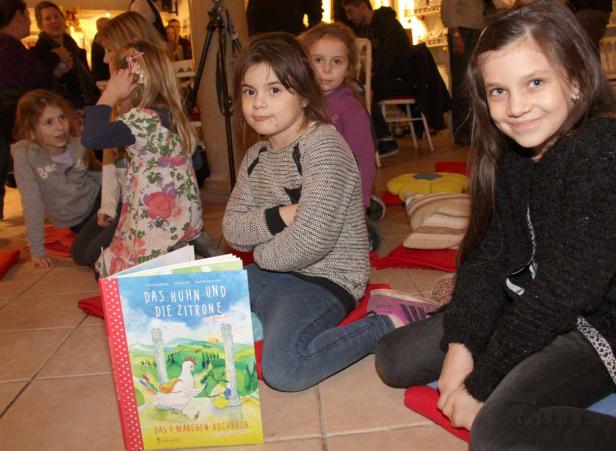 Mehrere Mädchen sitzen auf Kissen vor dem Buch „Das Huhn und die Zitrone auf Reisen“.