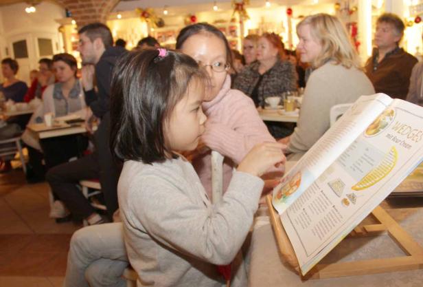 Ein Mädchen schaut mit einer Frau ein Kochbuch mit dem Rezept für Wedges an.