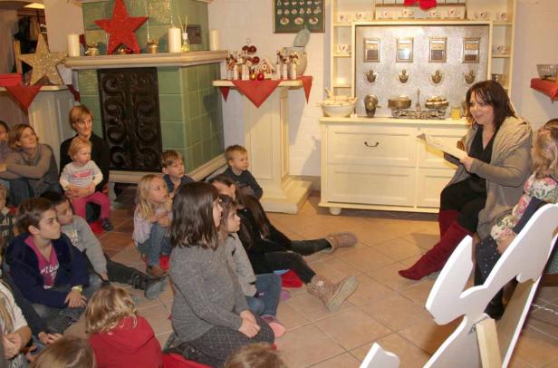 Eine Frau liest einer Gruppe von Kindern in einem weihnachtlich geschmückten Raum vor.