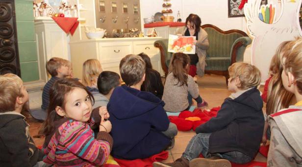 Eine Frau liest einer Gruppe von Kindern in einem Raum mit weihnachtlicher Dekoration eine Geschichte vor.