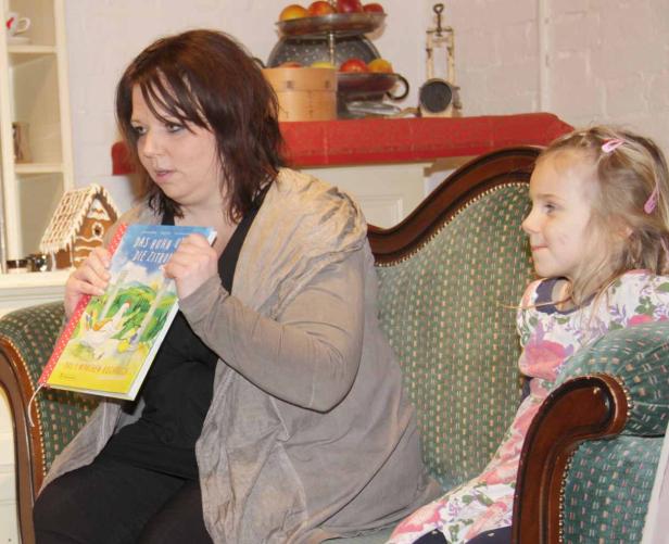 Eine Frau liest einem kleinen Mädchen aus dem Buch „Das Huhn und die Zitrone“ vor.