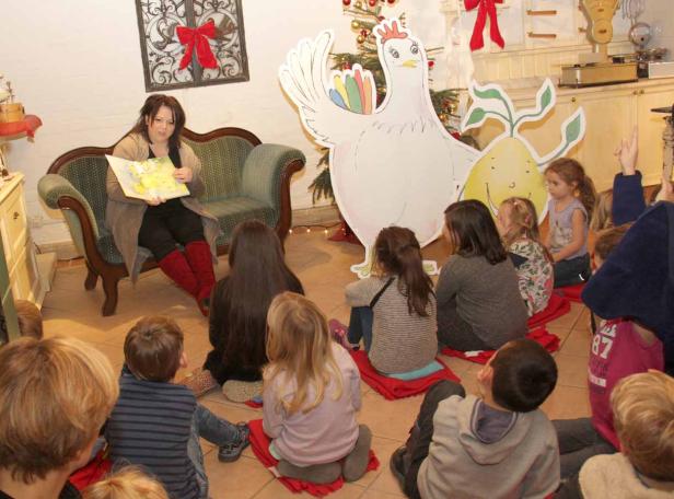 Eine Frau liest Kindern eine Geschichte vor, im Hintergrund eine große Hühnerfigur.
