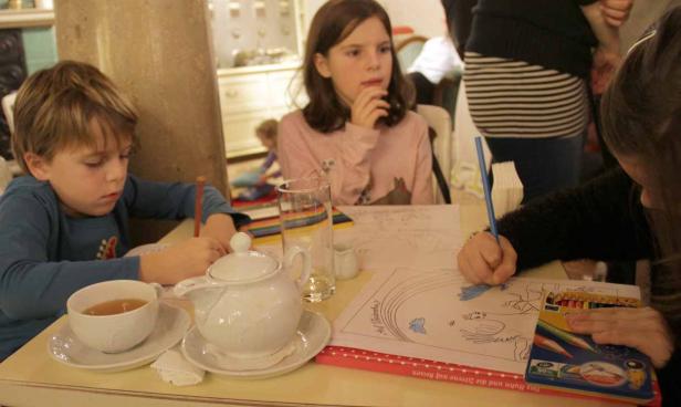 Kinder sitzen an einem Tisch, trinken Tee und malen Bilder aus.