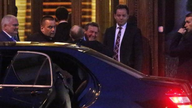 Gerhard Schröder steigt in ein Auto, umgeben von mehreren Sicherheitsleuten.