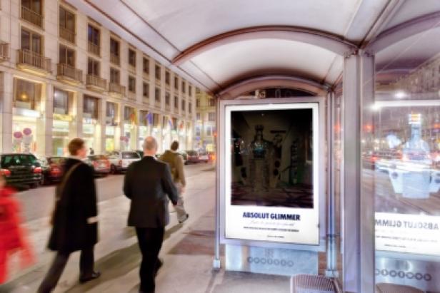 Eine Bushaltestelle mit einer Werbung für „Absolut Glimmer“ bei Nacht.